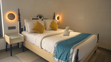 A bed with illuminated circular wall lamps on either side and a blue bed runner at Hotel Sonar Bangla, Mayapur.