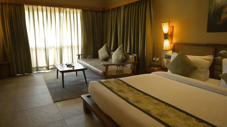 A hotel room featuring a bed,  a sofa area with a coffee table, and floor-to-ceiling curtains at Hotel Sonar Bangla, Sundarban.