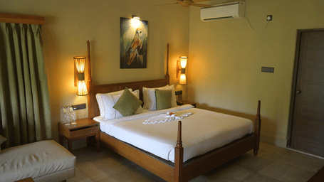 A double bedroom with a wooden bed frame, white linens, green pillows, and bedside lamps at Hotel Sonar Bangla, Sundarban.