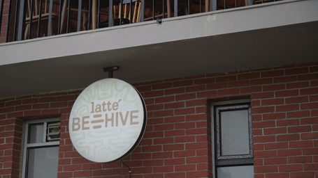A circular white sign for Latte Beehive mounted on a red brick wall below a balcony at Hotel Sonar Bangla, Sundarban.