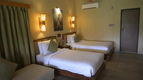 A bedroom featuring 2 single beds, a sofa, and olive green curtains next to a doorway at Hotel Sonar Bangla, Sundarban. 