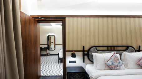 A modern guest bedroom featuring a large bed, wooden interiors, soft lighting, and a doorway leading to another bedroom | Hotel Sonar Bangla, Susunia