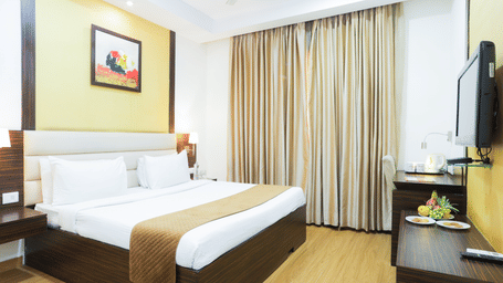 Well-furnished double bed room with elegant lighting, wooden flooring, and wall-mounted TV at Hyphen Premier Hotel, Meerut.