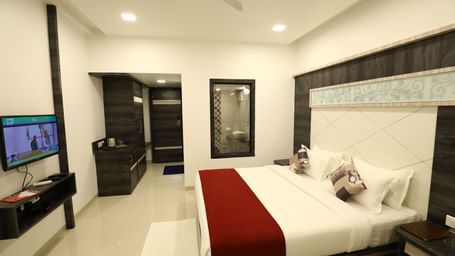 A room in Imperial Grande with a bed covered in white and red bedding, a television on a stand, and a mirror on the wall.