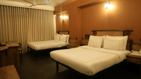 A bedroom at Infiniti Hotel, Indore featuring 2 double beds, hanging lights, curtains, and wooden furniture.