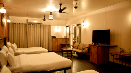A bedroom at Infiniti Hotel, Indore featuring 3 double beds, seating area, television, and ceiling lamps.