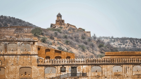 The exterior walls and bridge of Amber Fort, Jaipur, with a hilltop watchtower visible in the distance.
