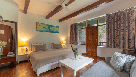 A double room layout featuring a comfortable bed, a grey couch, and floral patterned curtains - Johnson Lodge & Spa, Manali