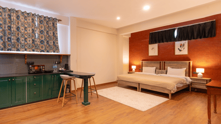 An open-plan studio apartment showing the green cabinetry of the kitchenette and the sleeping area with warm lighting - Johnson Lodge & Spa, Manali