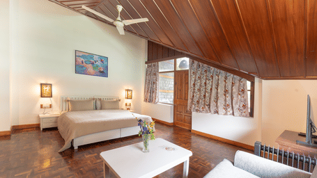 A spacious premium attic bedroom with polished wooden floors, white furniture, and a high timber-lined ceiling - Johnson Lodge & Spa, Manali