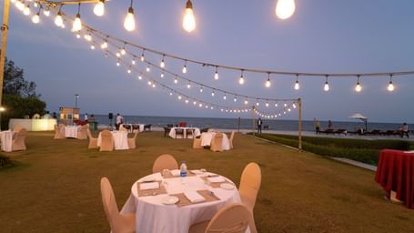 Round tables with white chairs set up on a lawn under string lights - Kaldan Samudra Palace