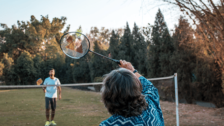 Two people playing badminton in a manicured lawn with a net in the centre - Karma Lakelands.