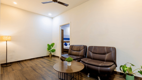 Spacious and separate living room in the Studio Room of Kove Smart Stays furnished with a multi-seater sofa with centre table, potted plants, and a lamp.