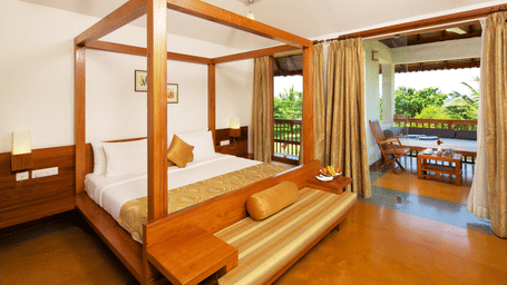A hotel room featuring a wooden 4-poster bed and an open doorway leading out onto a private balcony with outdoor seating | Le Pondy