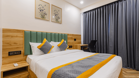 A bedroom at Lemonridge by Monday Hotels - KPHB featuring a large bed, green headboard, framed twin pictures, grey window curtains, and a side study table.