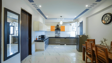 Open-plan apartment view showing a dining table set in the foreground leading towards a modern fitted kitchenette.