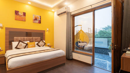An image of a bedroom with a double size bed, a bedside table, and a glass slider door leading to the balcony - Lime Tree Hotel & One BHK, Noida Sector 50