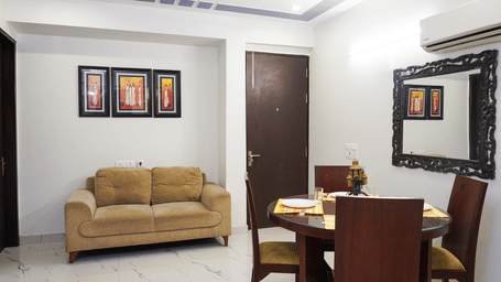 Suite of Lime Tree Hotels & Service Apartment Private Limited featuring a beige sofa, a dining table, and framed wall art.