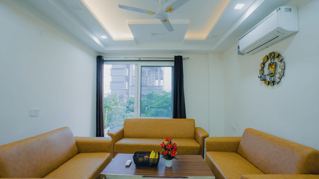 Living room of Lime Tree Hotels & Service Apartment Private Limited featuring a yellow sofa, a ceiling fan, and a wall clock.
