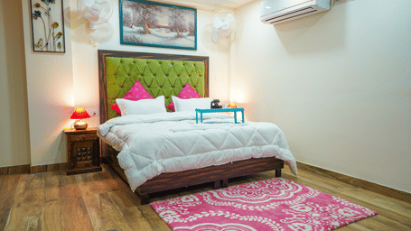 Bedroom of Lime Tree Hotels & Service Apartment Private Limited featuring a green headboard, pink cushions, and a patterned rug.