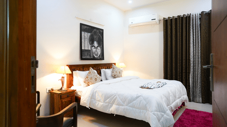 Bedroom of Lime Tree Hotels & Service Apartment Private Limited featuring white bedding with a maroon throw and framed wall art.