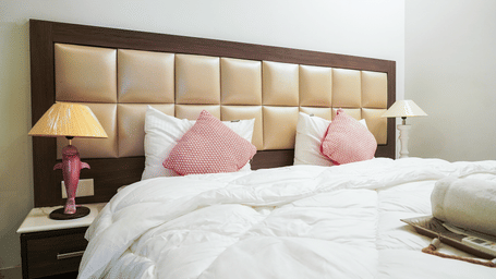 Bedroom of Lime Tree Hotels & Service Apartment Private Limited featuring a padded headboard, pink cushions, and bedside lamps.