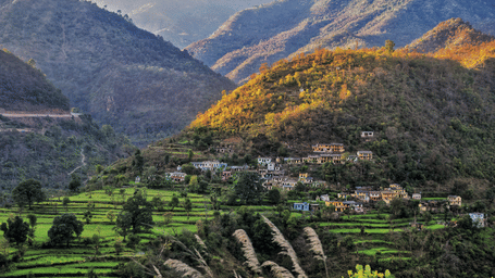 Terraced green fields featuring a hillside village and mountains in the background.