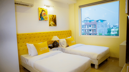 Bedroom of Lime Tree Hotels & Service Apartment Private Limited featuring twin beds, a yellow headboard, and framed wall art.