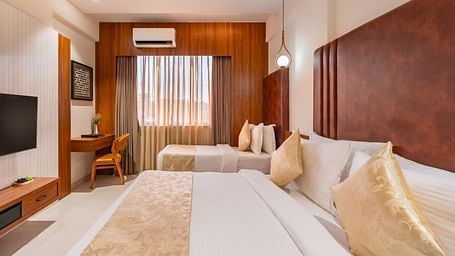 A hotel room offers a large bed and a smaller bed, along with a desk and a mounted television for guests - Lords Eco Inn Ambaji.