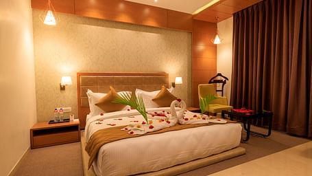 A warmly lit hotel room at Lords Eco Inn Apple Gate features a decorated double bed, bedside tables, a chair, and brown curtains.