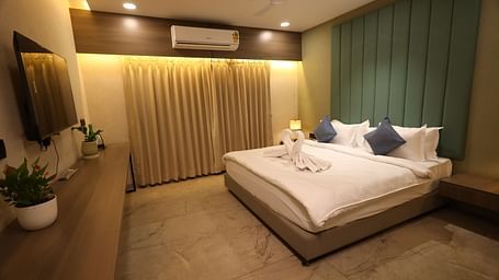 A hotel room in Navsari features a bed with folded towels, bedside lamps, and a long dresser with plants - Lords Eco Inn Navsari.