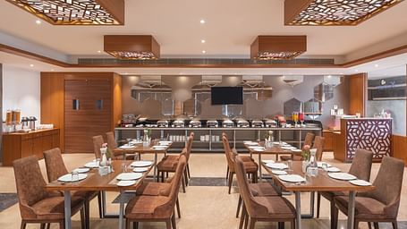 The spacious restaurant at Lords Inn Udaipur is set with multiple tables and chairs, featuring a buffet area in the background.