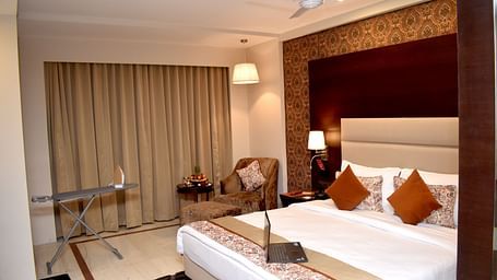 A hotel room features a bed with a laptop and bedside lighting at Lords Plaza Surat.