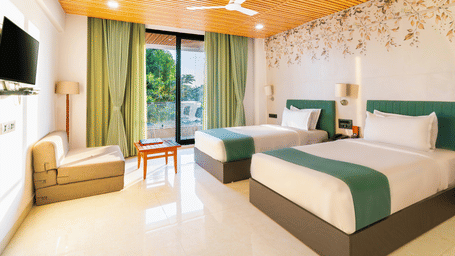 Bright twin bedroom at Lords SKD Resort, Salangpur, featuring teal accents, a sofa, and sliding doors leading to a balcony.