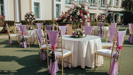 Outdoor banquet table setup with floral arrangements and purple chair sashes.