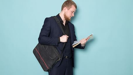 A businessman in a suit carrying a bag and holding documents in his hand.