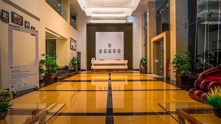 A brightly lit hotel hallway with polished floors and plants | Mansha Hotels