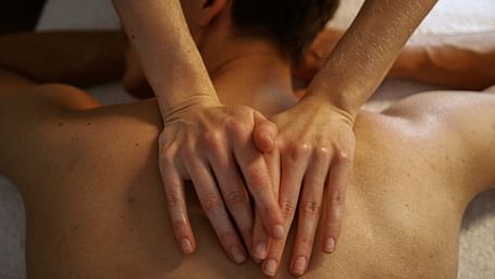 A massage therapist applying gentle pressure on a patient's back using both hands.
