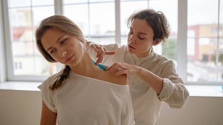 A therapist applying kinesiology tape to a patient's shoulder for support and pain relief.