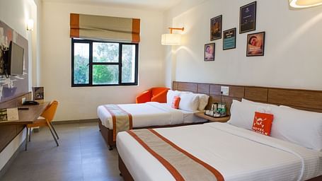 a brightly lit bedroom with two double beds facing towards the TV table - Max Hotel Jabalpur
