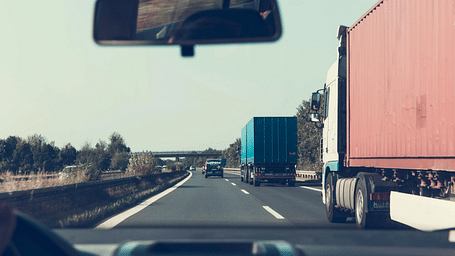 View from inside a moving car on a highway, passing container trucks under a clear sky.
