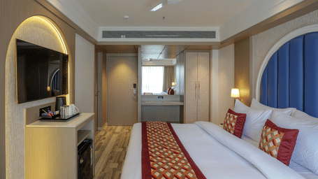 A room at Melorin with a large bed, spreads, pillows, a televisio, and a window.