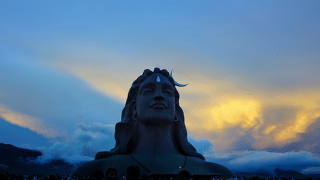 Adiyogi Shiva statue silhouetted against a dramatic sunset sky, with the Velliangiri Hills forming a striking backdrop at dusk at Isha Temple in Coimbatore