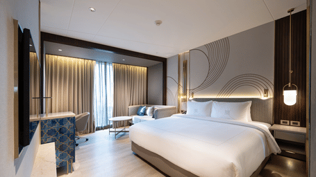 A hotel accommodation in Coimbatore featuring a plush bed facing the TV on the wall and a large ceiling-to-floor window covered with curtains at Merlis Hotel, Coimbatore