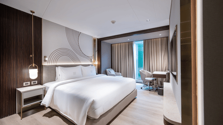  A contemporary hotel bedroom featuring a large double bed, modern lighting, and a small desk area at Merlis Hotel, Coimbatore.