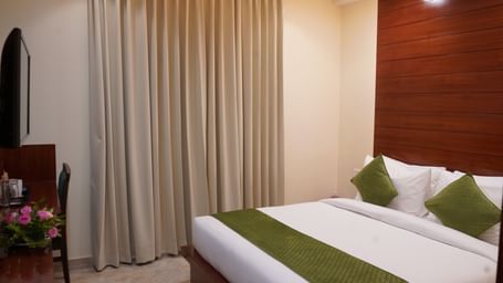 A wide shot of a hotel room bed with a white comforter and green accents.