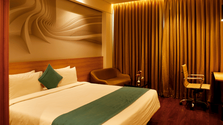 The deluxe room in the hotel during night time with the warm lights turned on featuring a plush bed, chairs, and big curtain windows.