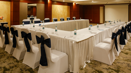 A banquet hall with a boardroom setting in u-shape with the tables and chairs covered with white covers.