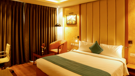 Luxury hotel room interior with warm lighting, a comfortable bed, and wooden flooring.