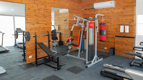 A gym floor featuring a barbell bench press station, a punching bag, a multi-station weight machine, and wall mirrors.